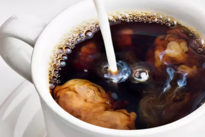cup of coffee with creamer being pored in