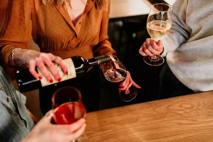 A seated woman pouring herself a glass of red wine.