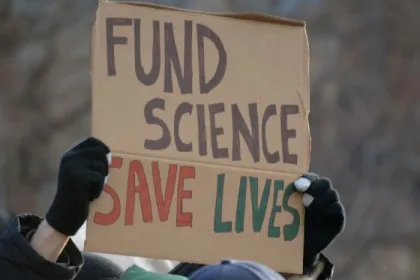 A protest sign reads "FUND SCIENCE SAVE LIVES"