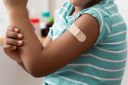 A Black child shows off their arm with a bandage over a vaccine injection site