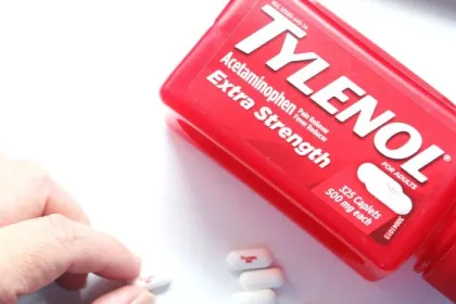 A hand picks up a tablet of Tylenol from a white surface beside a red bottle of Tylenol Extra Strength acetaminophen, which RFK and Trump wrongly assert causes autism.