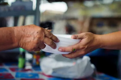 Closeup of a person handing a bowl of food to another person.