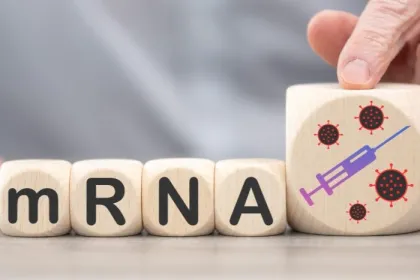 Wooden blocks spelling "mRNA" and a larger fifth block displaying a painted syringe on a table