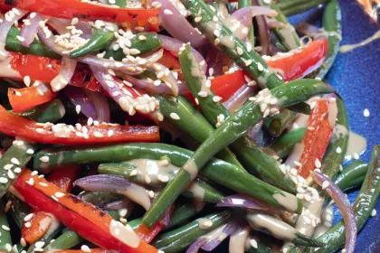 green beans and sliced peppers covered in sauce and sesame seeds
