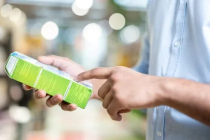 A man in a blue shirt is holding a green box and pointing at the details printed on it while shopping.