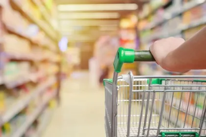 A grocery cart with a green handle in a grocery store aisle