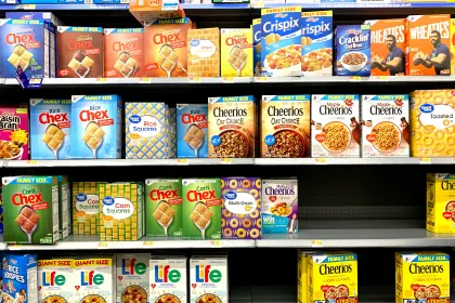 A cereal aisle displaying Cheerios variations, Chex, Wheaties, Life Cereal, and more.