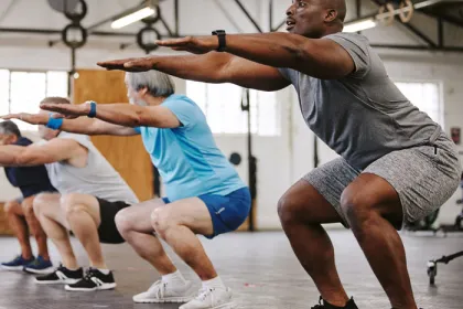 4 older men holding a squat in the gym
