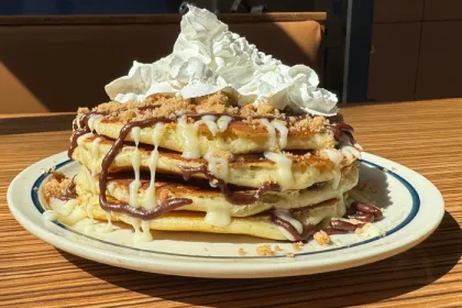 stack of 4 pancakes drizzled with chocolate icing, brown sugar and topped with whipped cream