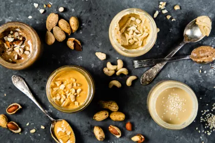 overhead shot of jars of different nut and seed butters with spoons on grey background