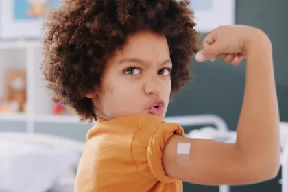 young child flexing muscles showing off a band-aid on their vaccine sight