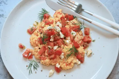 white plate with scrambled eggs, tomatoes and fetta and fork and knife