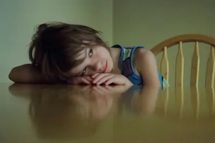 A little girl resting her head on an empty dining table. 