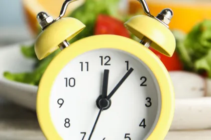 old yellow alarm clock in front of a plate of salad