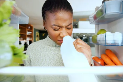 woman sniffing milk carton inside a fridge