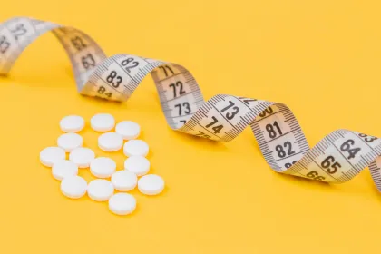 A measuring tape and weight loss pills on a yellow background