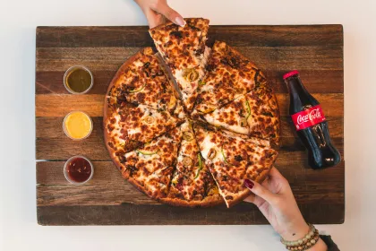 Overhead view of a pizza and bottle of soda on a cutting board