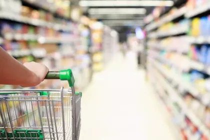 A shopper with grocery cart looking down a long supermarket aisle