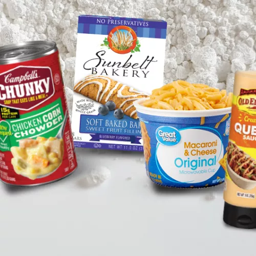 Canned soup, boxed mac & cheese, breakfast bars, and queso--packaged foods containing titanium dioxide--against a background of the powdered white substance.