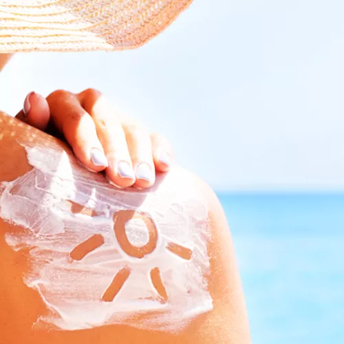 person rubbing sunscreen on their shoulder on a sunny day.