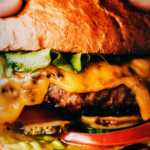 Close up of burger with cheese, pickles, tomato and lettuce.