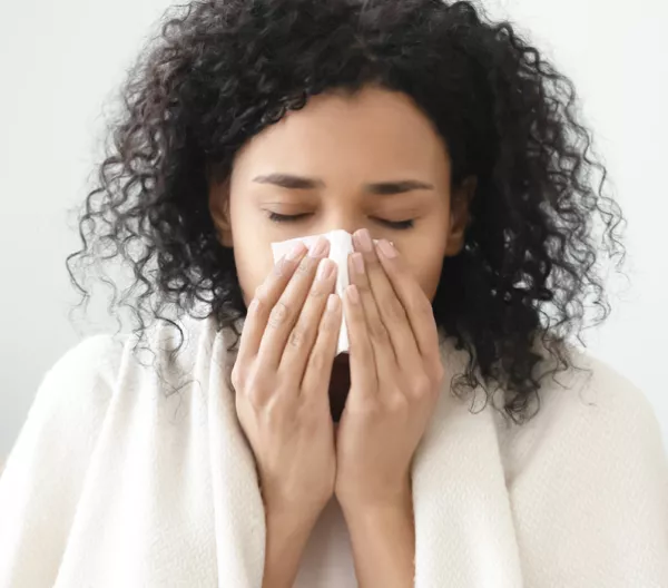 woman with blanket around her shoulders blowing her nose