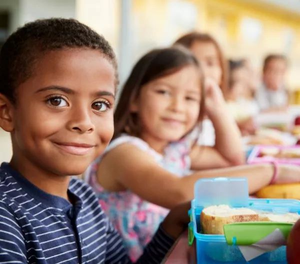 Young students enjoy a healthy, dye-free school lunch at a table and smile at camera