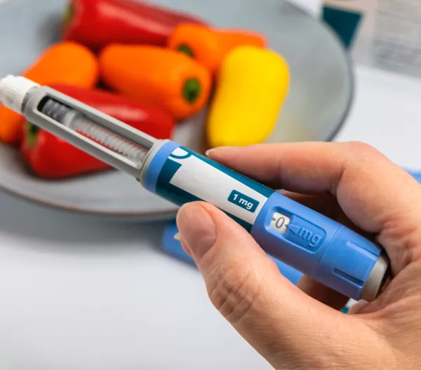 hand holding an obesity medication applicator with bell peppers in the background