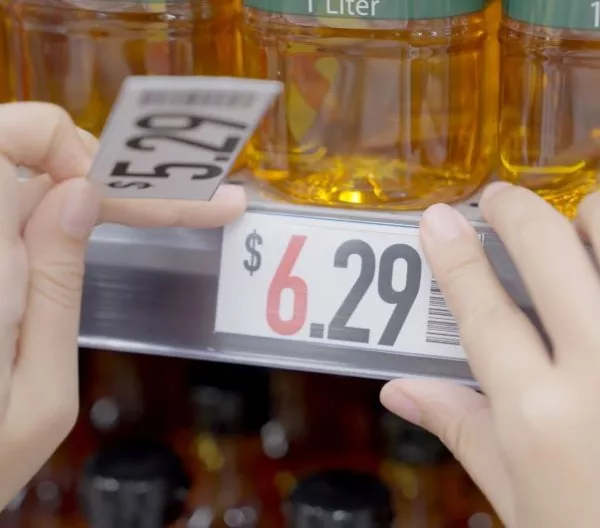 Closeup of grocery store worker increasing prices on cooking oil from $5.29 to $6.29. Rising food costs concept.