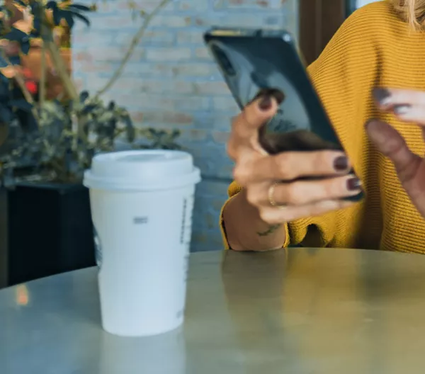 person looking at phone sitting at a cafe table with to-go coffee cup