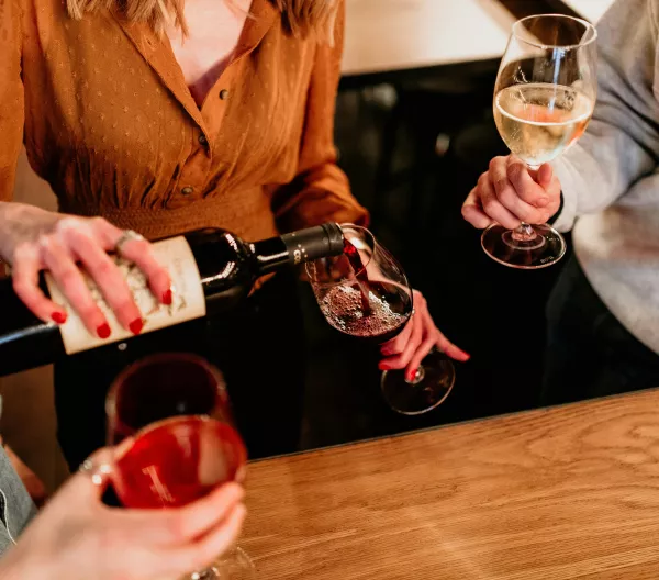A seated woman pouring herself a glass of red wine.