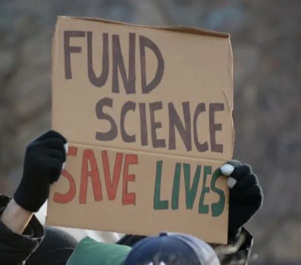 A protest sign reads "FUND SCIENCE SAVE LIVES"