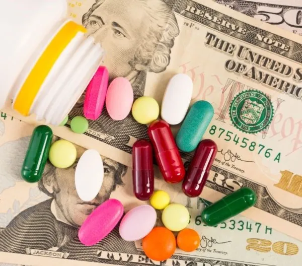 Money with a handful of supplements and tablets on top.