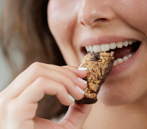 woman taking a bite of granola or protein bar