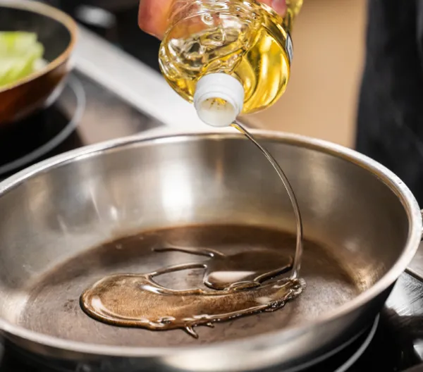 oil being pored from bottle into stainless steal pan