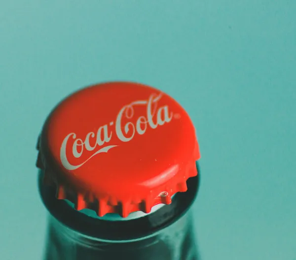 A red Coca-Cola bottle cap against a sky blue background