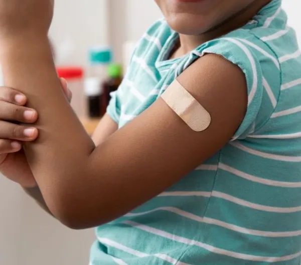 A Black child shows off their arm with a bandage over a vaccine injection site