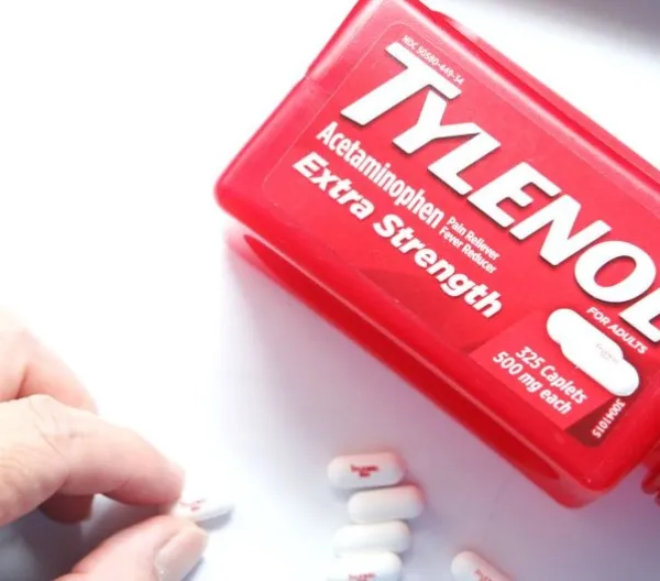 A hand picks up a tablet of Tylenol from a white surface beside a red bottle of Tylenol Extra Strength acetaminophen, which RFK and Trump wrongly assert causes autism.