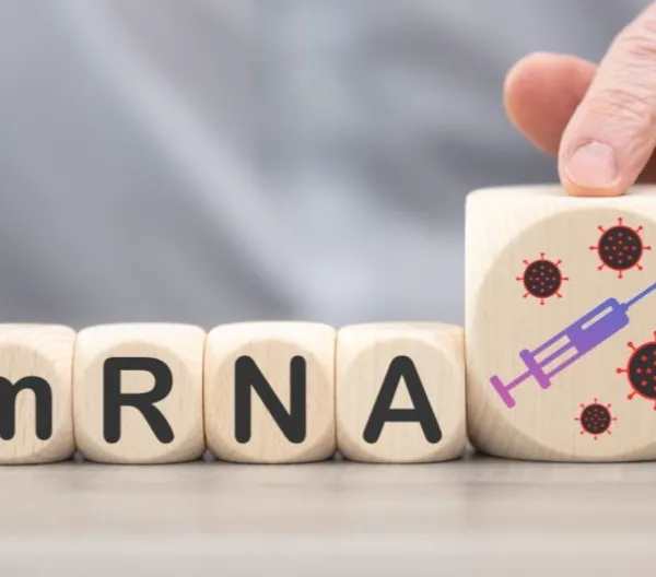 Wooden blocks spelling "mRNA" and a larger fifth block displaying a painted syringe on a table