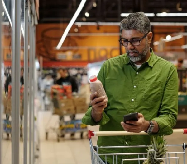 A man ina  green shirt reads the label on a packaged food product in a grocery store
