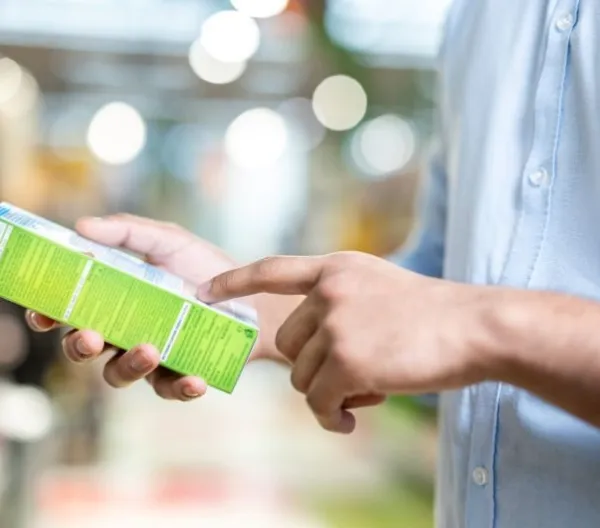 A man in a blue shirt is holding a green box and pointing at the details printed on it while shopping.