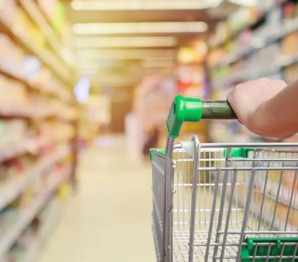 A grocery cart with a green handle in a grocery store aisle