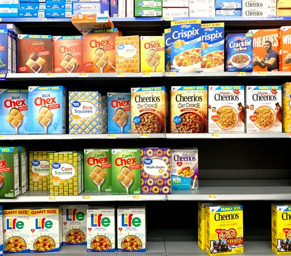 A cereal aisle displaying Cheerios variations, Chex, Wheaties, Life Cereal, and more.