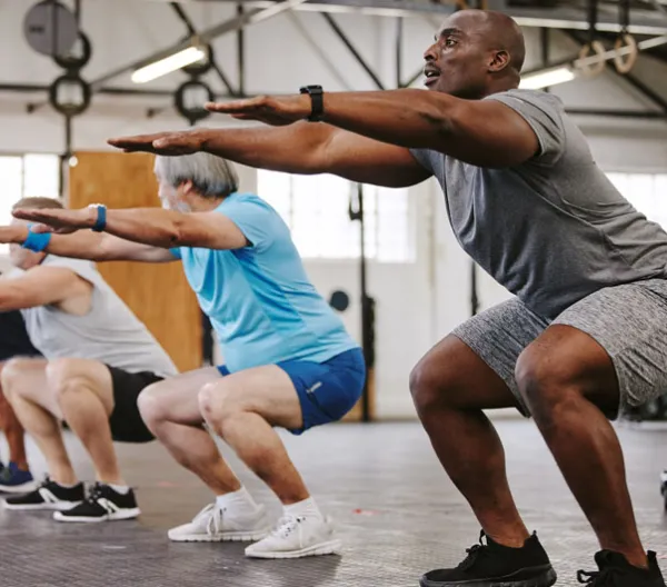 4 older men holding a squat in the gym