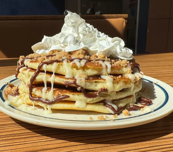 stack of 4 pancakes drizzled with chocolate icing, brown sugar and topped with whipped cream