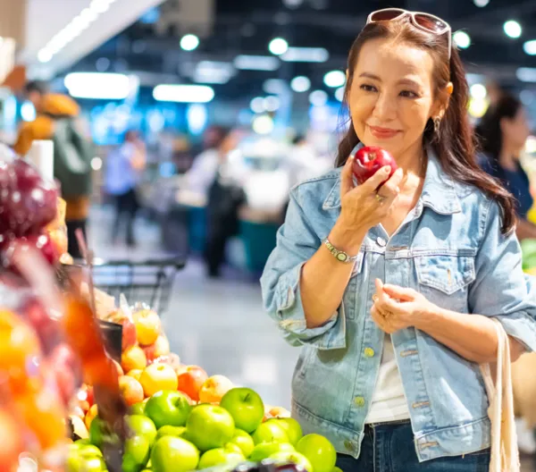 woman at grocery store holding a apple in the produce section