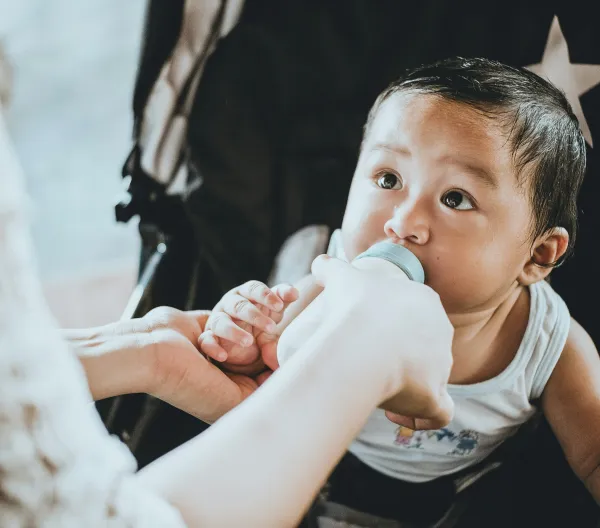 A baby in a stroller being fed from a bottle.