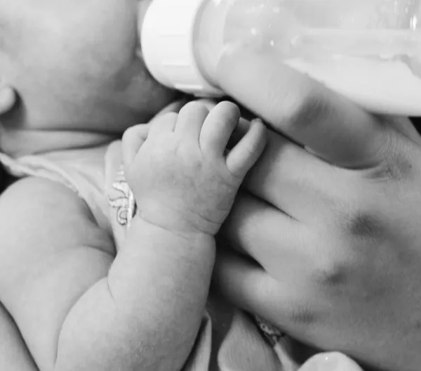An infant drinking from a bottle in black and white