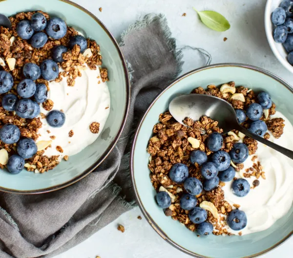 two blue bowls filled with yogurt, granola and blueberries