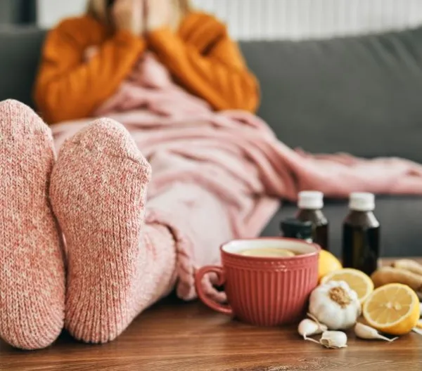 Feet wearing warm socks on a low table beside cold medicine and home remedies